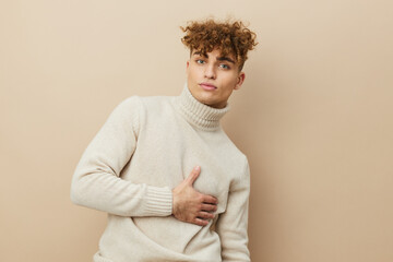 portrait of a handsome man with curly hair, standing on a beige background in a light turtleneck, holding his hand on his body, looking pleasantly into the camera.