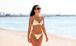© Syda Productions - people, summer and swimwear concept - happy smiling young woman in bikini swimsuit walking along beach