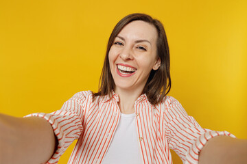 Wall Mural - Close up young happy smiling cheerful woman she 30s wears striped shirt white t-shirt doing selfie shot pov on mobile cell phone isolated on plain yellow background studio. People lifestyle concept.