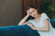 © ViDi Studio - Young sad sick ill woman she 20s wearing casual clothes mint t-shirt prop up head suffer from headache close eyes sit on blue sofa indoor rest at home in own room apartment. People lifestyle concept.