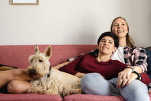 Caucasian Woman Lying On Happy Girlfriend's Shoulder While Relaxing With Scottish Terrier On Sofa