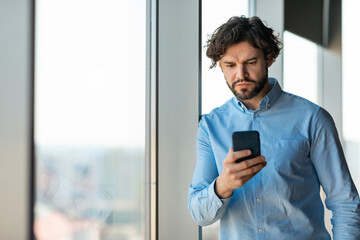 Wall Mural - Serious middle aged businessman using smartphone, working online, reading marketing report at office, copy space