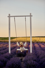 Wall Mural - young beautiful pregnant girl on a swing in a lavender field at sunset