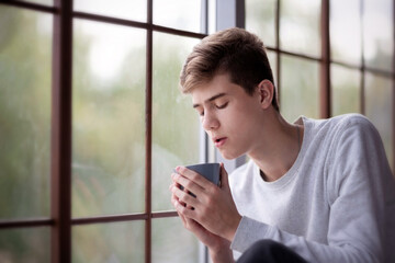 Wall Mural - Young man with a mug near the window