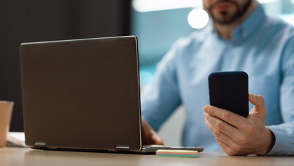 Sticker - Unrecognizable mature businessman typing on smartphone, using laptop at office, selective focus. Banner with free space