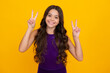 Teenager child girl showing fingers victory sign. Number two, v-sign symbol isolated on yellow background. Happy girl face, positive and smiling emotions.