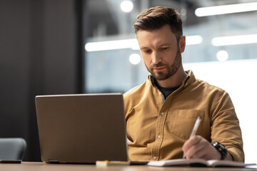 Poster - Serious Businessman Using Laptop Computer Taking Notes In Modern Office