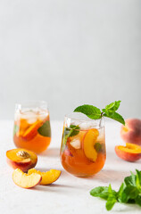 Summer cold peach fizz cocktail or iced tea with mint. Two glasses with peach lemonade on a white background. Summer refreshing drink recipe. Homemade fruit tea with ice. Restaurant menu. Copy space