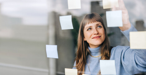 young female entrepreneur sticking adhesive notes to a glass wall