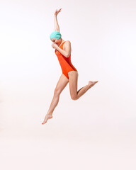 Portrait of young woman in swimming suit and cap jumping into water isolated over grey studio background