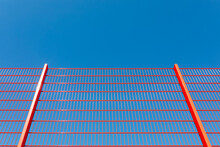 A Fragment Of A Modern Fencing, A Metal Red Fence Against A Blue Sky Background.