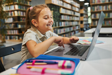 Wall Mural - Happy student doing her homework using laptop in after school club at primary school. Back to school. Child using technology on computer science class. Learning from educational application at school