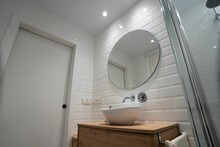 Low Angle Shot Of Circle Mirror On White Wall With Sink And Water Tap Below In Bathroom
