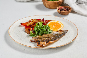 Fish dish - roasted dorado fillet with vegetables. Grilled fish fillet and roasted paprika, tomatoes and onion. Roast dorado fillet with garnish, greens and lemon on ceramic plate.