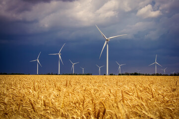 Wind turbines and agricultural field on a summer cloudy day. Energy production, clean and renewable energy.