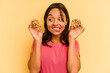 Young hispanic woman holding cookies isolated on yellow background