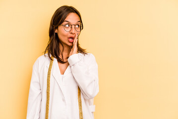 Wall Mural - Young nutritionist hispanic woman isolated on yellow background is saying a secret hot braking news and looking aside