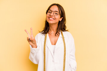 Wall Mural - Young nutritionist hispanic woman isolated on yellow background showing number two with fingers.