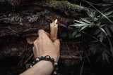Fototapeta  - burning candles and a womans hand with a bracelet on a dark natural background. pagan wiccan, slavic traditions. Witchcraft, esoteric spiritual ritual for mabon, samhain. autumn equinox festival