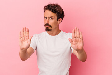 Young caucasian man isolated on pink background standing with outstretched hand showing stop sign, preventing you.