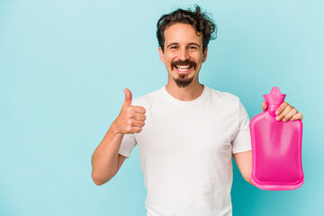 Wall Mural - Young caucasian man holding a water bag isolated on blue background smiling and raising thumb up