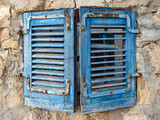 Fototapeta  - a window covered with old blue wooden blinds in the wall of an old house.