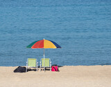 Fototapeta  - Multi-colored bright sunny umbrella, two sun loungers on the Mediterranean coast. Israel.copy space