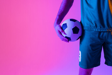 Caucasian male soccer player with football over neon pink lighting