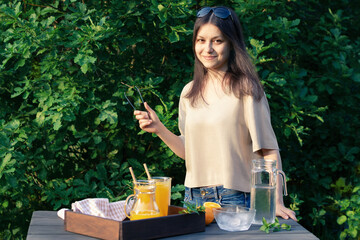 Wall Mural - Girl cooking summer orange cocktail with mint and ice cubes outdoors, selective focus