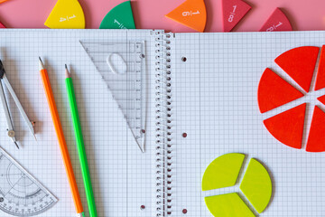 Wall Mural - Back to school background. Open notepad, fractions, chart, pencils on a pastel pink background. Close up parts of yellow math fractions. Back to school, fun study, mathematics