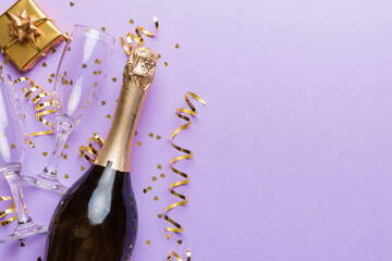 Bottle of champagne with colored glitter, confetti and gift box space for text on colorfull background, top view. Hilarious, christmas and birthday celebration