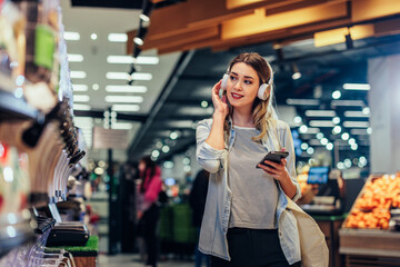 Wall Mural - Young woman in grocery using phone and listening music