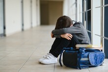 Upset Boy Sitting At School And Crying After Bullying By Pupils Classmates. The Child Covered His Face With His Hands And Cries.