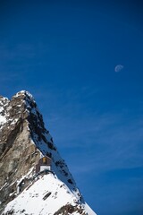 Sticker - Vertical shot of a snowy mountain summit against a blue sky with the moon