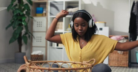 Wall Mural - Portrait of smiling young women folding clean clothes, sorting laundry before putting it in the washing machine, a student sitting on the bathroom floor listening to music on wireless headphones.