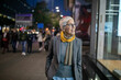 © Adam Radosavljevic - Smiling mature senior woman with short gray hair and eyeglasses walking on street, night scene in city