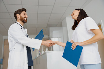 Wall Mural - Two doctors in uniform shaking hands standing in clinic hall near reception