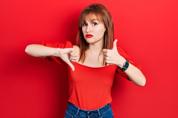 Canvas Print - Redhead young woman wearing casual red t shirt doing thumbs up and down, disagreement and agreement expression. crazy conflict