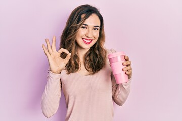 Poster - Young hispanic girl holding coffee doing ok sign with fingers, smiling friendly gesturing excellent symbol