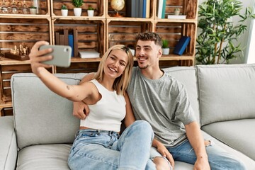 Poster - Young caucasian couple smiling happy making selfie by the smartphone at home.