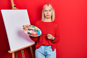 Poster - Beautiful blonde woman standing drawing with palette by painter easel stand skeptic and nervous, frowning upset because of problem. negative person.