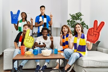 Poster - Group of friends supporting football team watching tv al home sitting on the sofa surprised with an idea or question pointing finger with happy face, number one