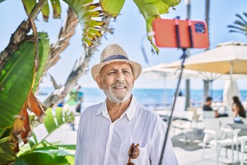 Canvas Print - Senior man wearing summer hat making selfie by the smartphone at seaside