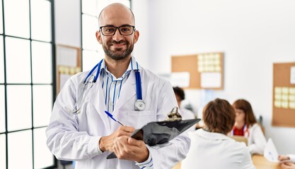 Sticker - Group of young doctor working at the clinic office. Man smiling happy writing on clipboard.