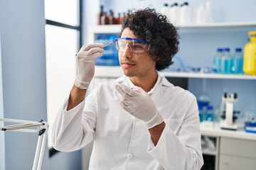 Sticker - Young hispanic man wearing scientist uniform holding sample with tweezer at laboratory