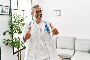 Sticker - Middle age hispanic man wearing doctor uniform and stethoscope at waiting room approving doing positive gesture with hand, thumbs up smiling and happy for success. winner gesture.