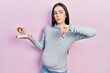 Beautiful woman with blue eyes expecting a baby, holding anatomic fetus with angry face, negative sign showing dislike with thumbs down, rejection concept
