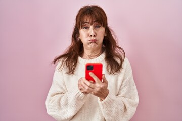 Canvas Print - Middle age hispanic woman using smartphone typing message puffing cheeks with funny face. mouth inflated with air, catching air.