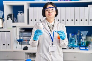 Sticker - Young asian woman working at scientist laboratory puffing cheeks with funny face. mouth inflated with air, catching air.