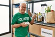 © Krakenimages.com - Senior man wearing volunteer uniform holding canned food at charity center